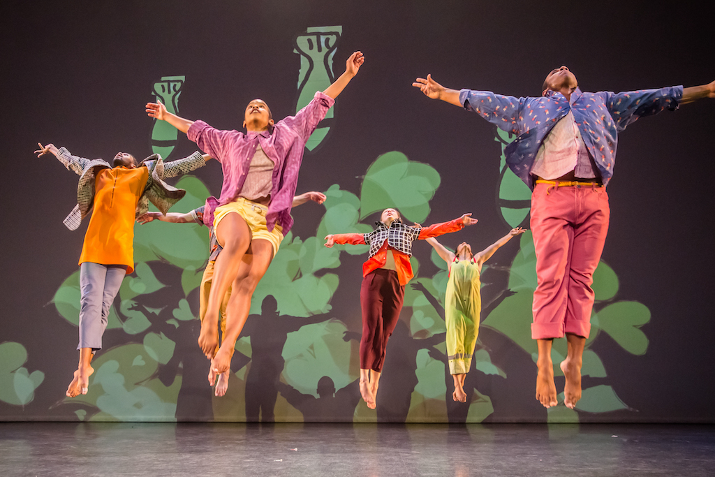 Photo of dancers performing on stage leaping in midair